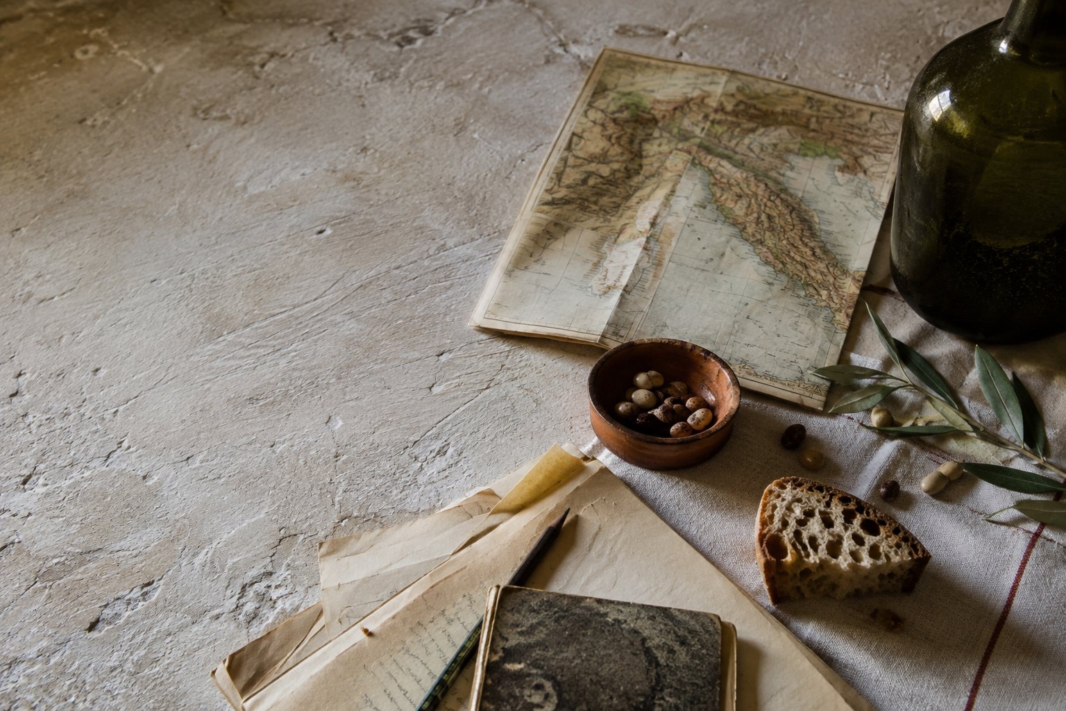 Editorial illustration of a worktable with a map of Italy, notes, bread, beans and olive branches